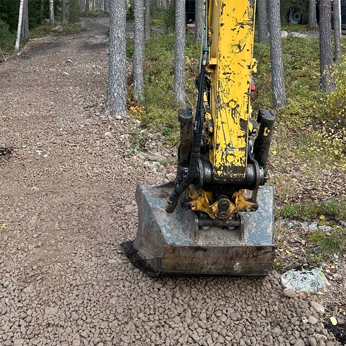 Keltaisen kaivinkoneen kauha soratiellä metsässä